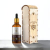 Amber glass dropper bottle labeled “Amigos Power Moroccan 100% Natural, Organic Argan Oil” standing next to an engraved wooden box featuring the brand’s logo. The back of the box displays detailed product information and ingredients in English and Greek.
